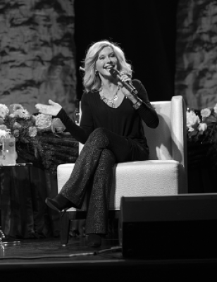 A blonde women speaking into a microphone while sitting on stage
