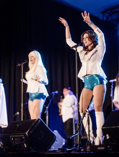 Two female performers captivating the audience on stage, wearing white tops and tight blue shorts