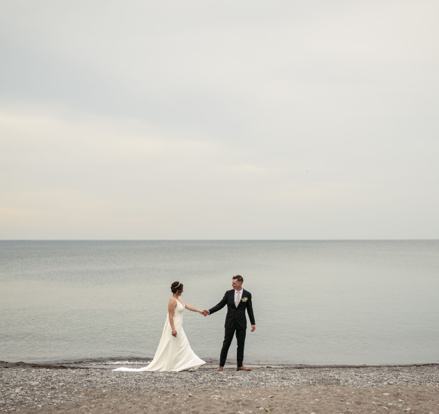 Newlywed couple embraces, holding hands on a serene beach