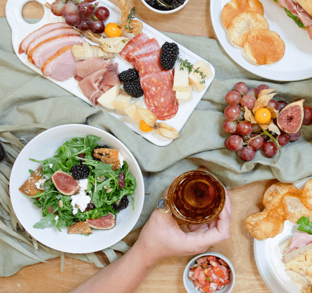A delectable charcuterie board featuring a variety of ingredients, including a colorful salad, juicy grapes, crispy chips, sweet figs, and ripe tomatoes, offering a delightful blend of flavors and textures